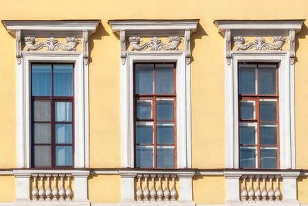 三个长方形窗户，在黄色墙壁的背景上有一个棕色的框架，有一个浮雕。 从圣彼得堡的一系列窗户。