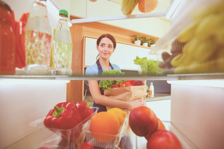 女性站附近打开冰箱充分的健康食品，蔬菜和水果的画像。女性肖像