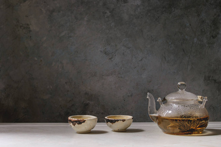 热绿茶在两个传统的中国粘土陶瓷杯和玻璃茶壶站在白色大理石桌子上。