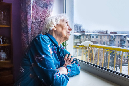 一位孤独的老妇人坐在他家的窗户附近，望着，做梦