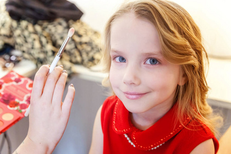 化妆大师的手为小漂亮女孩模特涂上眼影。 专业化妆由艺术家申请。 在过程中弥补细节。 时尚儿童美容院摄影概念