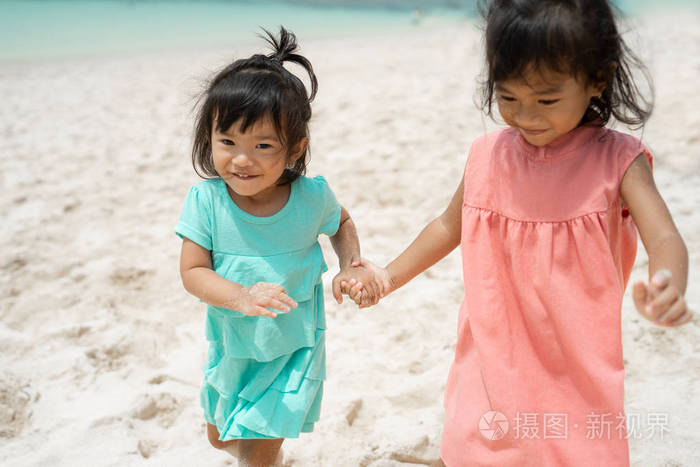 两个小女孩在海边走在白沙上时牵手