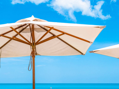 带椰子棕榈树的白色雨伞，带海洋，蓝天背景，供旅行和度假使用