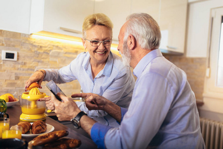 一对老夫妇在家厨房里吃着美味的早餐，忙着看数码平板电脑