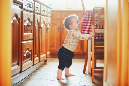 女婴站在厨房的地板上，拿着家具。 小孩子在家里大吵大闹