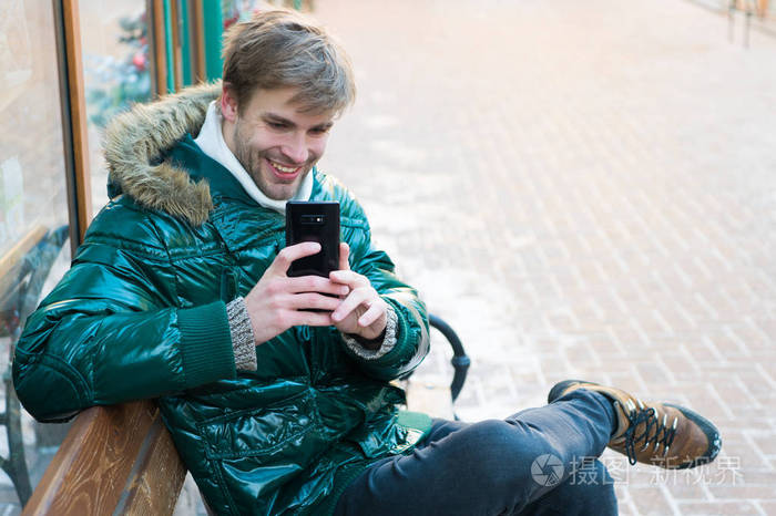 希普斯特在冬天使用智能手机.男人英俊拿着智能手机.男坐板凳互动智