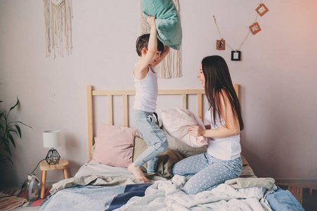 快乐的母子儿子一大早就在床上玩枕头大战。 家庭休闲生活方式系列。