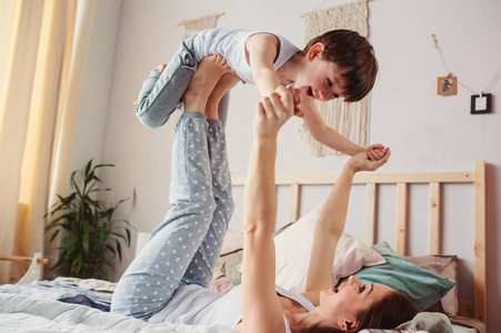 妈妈和快乐的蹒跚学步的儿子在床上做早操。 幸福的家庭在家玩耍