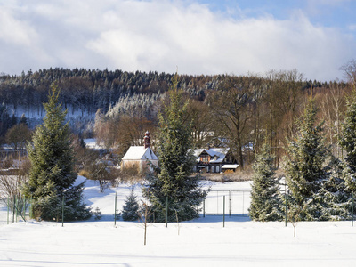 村庄旅行的冬天看法与教堂, 木结构的小屋和树, 雪覆盖了农村风景与在卢兹克霍里山