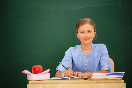 回到学校.有趣的漂亮女孩坐在教室里对着黑板。 有书和配件的孩子在学校。 教育概念