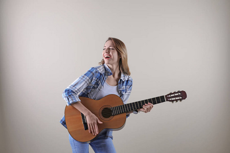 在灰色背景下弹声吉他的年轻女子