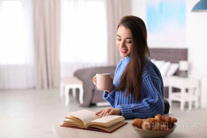 年轻的女人在桌子上喝咖啡和看书,在室内空间发短信.