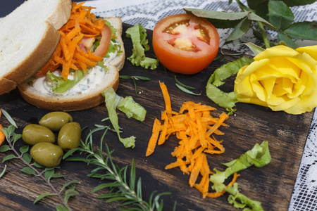 健康的素食三明治，胡萝卜番茄生菜和香料，用黄玫瑰放在木板上。