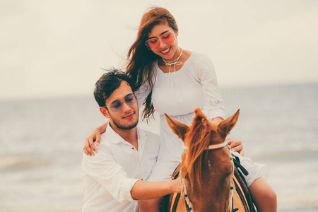 年轻夫妇在暑假去蜜月骑马去海滩。