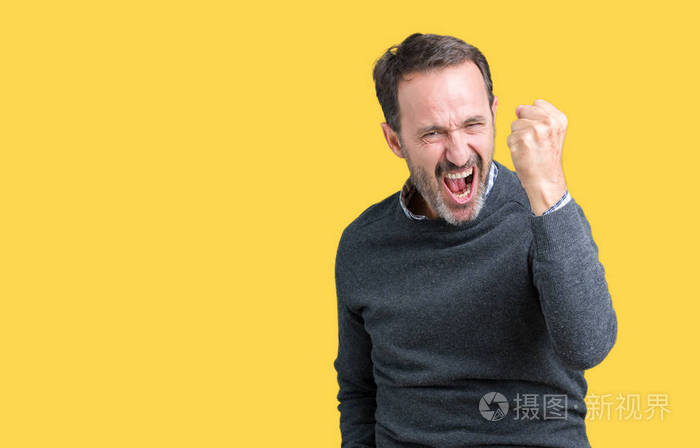英俊的中年老人穿着一件毛衣,在孤立的背景下愤怒和疯狂地举起拳头