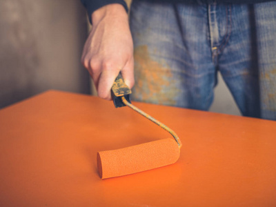 s hand is using a paint roller on an orange surface