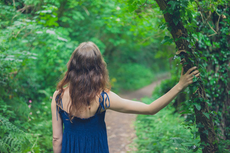一个年轻的女人站在森林里，手放在树上