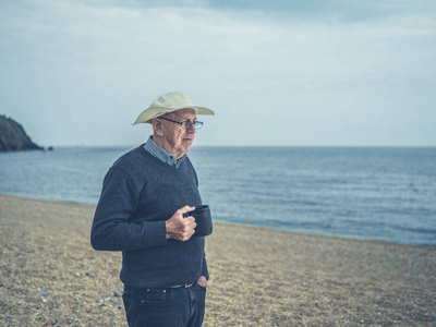 一位老人正站在海滩上，手里拿着一杯饮料