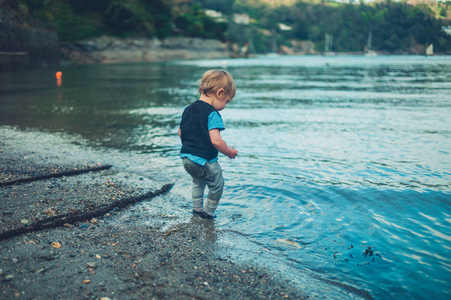 一个可爱的蹒跚学步的小男孩正在水边玩耍