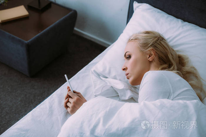 孤独的女人躺在床上,在家里使用智能手机