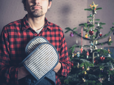 一个戴着烤箱手套的年轻人站在圣诞树旁