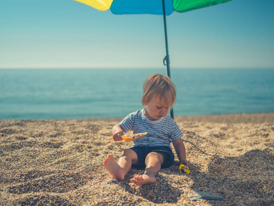 夏天，一个小蹒跚学步的孩子独自坐在沙滩上的阳伞下