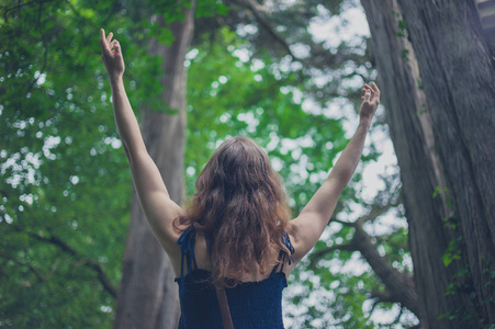 一个年轻的女人在森林里快乐地举起她的手臂