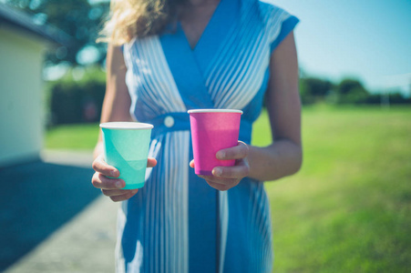 一个年轻的女人站在草坪上，夏天拿着两个纸杯