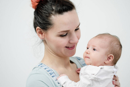 穿着粗斜纹棉布工作服的年轻女性母亲抱着一个婴儿。工作室的白色背景
