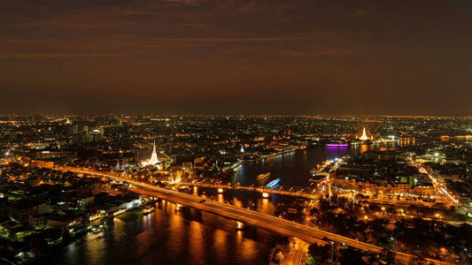白祈祷宝塔纪念桥和PhraPokKlao桥，夜间有潮法拉河的建筑物和曲线。 泰国曼谷市中心的城市。
