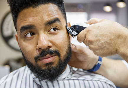 理发店用专业的电动剪子机剪下的黑人青年男子。男子美容的概念。