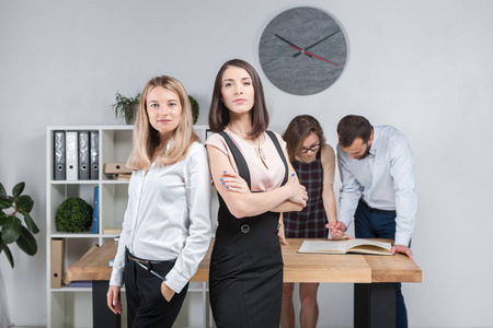 在办公室进行业务团队合作和谈判。 一群4名高加索人在房间里处理文件。 两位年轻的女老板在公司员工的背景下摆姿势。