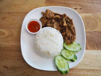 木制桌子上泰国快餐的俯视图。 米饭和炒猪肉，黄瓜和番茄酱在白板上。