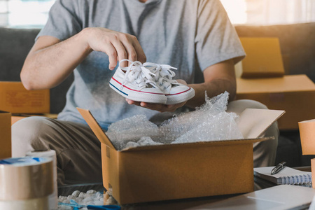亚洲企业家青少年正在携带婴儿鞋，并放入纸板箱客户交付产品在家里。