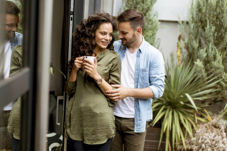 幸福的年轻可爱的一对相爱的夫妇拥抱在一起，在家门口的窗户边喝咖啡