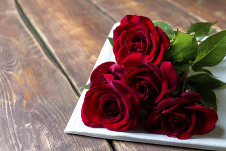 木桌上白色布上的五朵红玫瑰。 浪漫的概念。 平躺式顶部视图