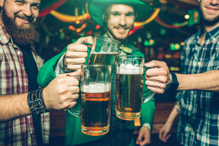 快乐快乐的朋友站在酒吧里欢呼。他们把一杯啤酒放得很近。人们微笑。他们穿着节日的紧身衣和绿色的西装