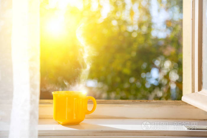 早上好! 窗户上的杯子有太阳和离焦的自然背景