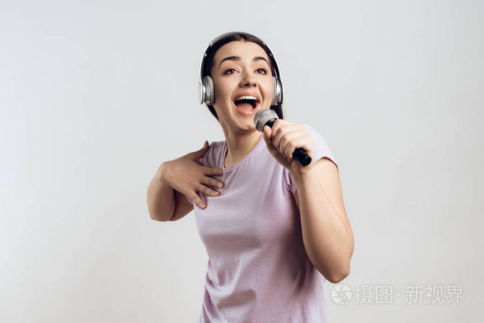 戴着耳机的年轻女孩用卡拉ok富有表现力地唱歌歌曲孤立在白色背景上