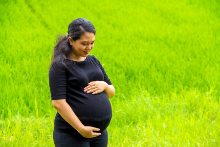 一位育龄妇女在乡村风景背景下观看她怀孕的腹部的户外肖像。