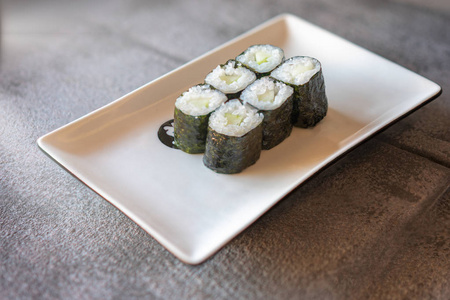 深灰石背景的长方形白色盘子上有黄瓜寿司