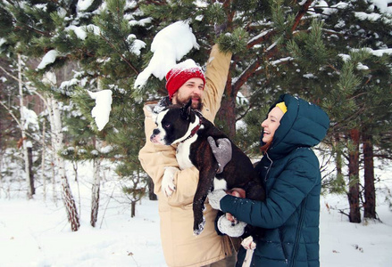 幸福的一对相爱的夫妇在雪地里和他的小狗玩。 积极美丽的年轻家庭穿着冬天的衣服。红发白种人女孩带着美丽的微笑，男人带着胡须