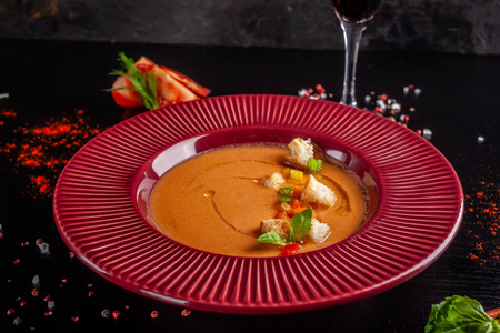 西班牙美食的概念。 新鲜西红柿的番茄汤加西番茄。 在餐馆的黑桌上，红色盘子里有漂亮的菜肴。 背景图像。 复制空间