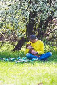 高加索人和他的有趣的狗达克松德在绿色的草地上玩，在一个野生盛开的樱桃下，在一个令人敬畏的春天玩。