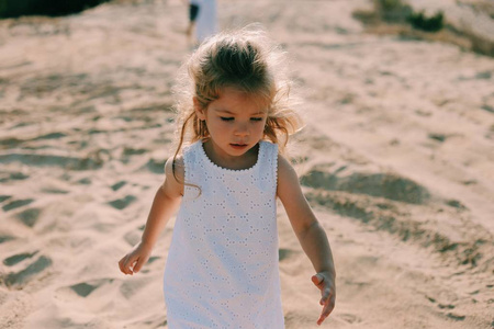 漂亮的小女孩在白色礼服有一个乐趣在沙滩背景