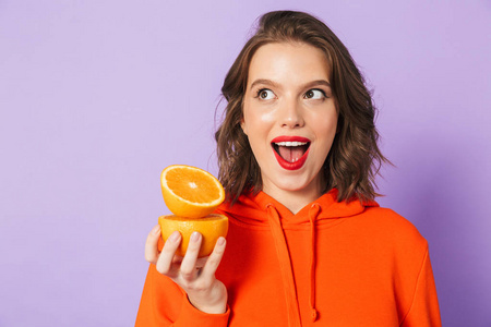 一个兴奋的美丽的年轻女人的形象，在紫色的背景墙上，抱着橙色的柑橘。