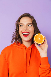 一个兴奋的美丽的年轻女人的形象，在紫色的背景墙上，抱着橙色的柑橘。