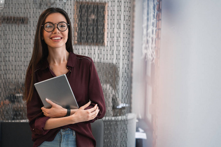 开朗的女人拿着平板电脑站在办公室里。 快乐商务女性在办公室休闲的肖像。