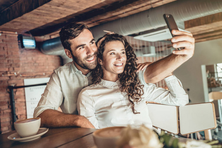 一起漂亮的夫妇在新智能手机上自拍。 相爱的夫妇花时间在咖啡馆里。
