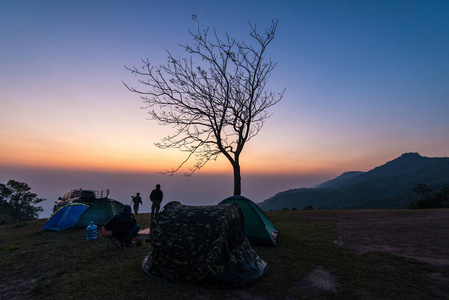日落或日出山上的帐篷区野山上的风景露营帐篷，带着黄昏的天空的游客。